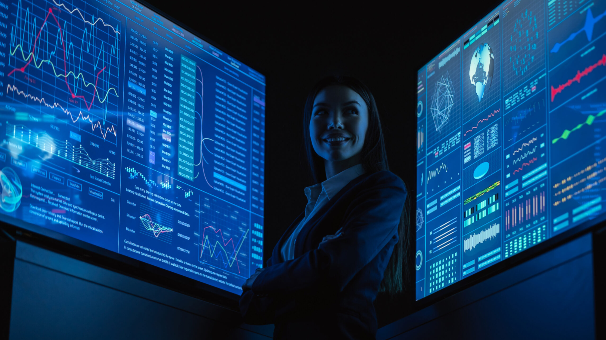 The smiling business lady standing between blue monitors in the dark office